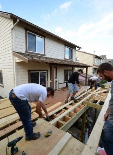 Crew installing new deck framing beside a house